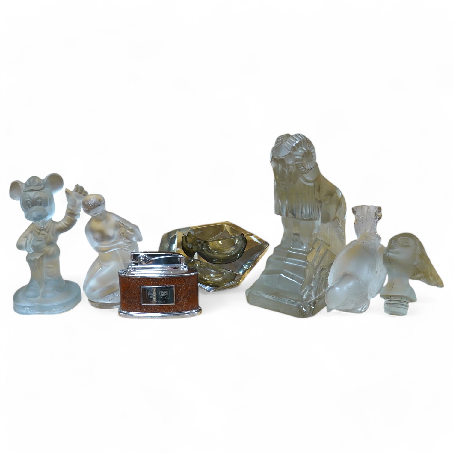 Two Lalique glass figures; a kneeling woman and deer group, a budgerigar, together with a Ronson ‘Senator’ Shell BP desk lighter, a Murano glass ash tray, an Art Deco style glass ram, etc. (7). Condition - poor to fair.